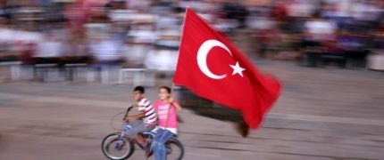 HATAY, TURKEY - JULY 30: Two Children wave Turkish flag as they ride on bicycle as people gather to protest against July 15 failed military coup attempt, at Iskenderun district of Hatay, Turkey on July 30, 2016. Turkish officials accuse U.S.-based Turkish citizen Fetullah Gulen plotting to overthrow the government of President Erdogan as the culmination of a long running campaign to infiltrate Turkish institutions including the military, the police and the judiciary. (Photo by Burak Milli/Anadolu Agency/Getty Images)